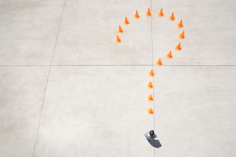 Traffic cones forming question mark with woman at point standing
