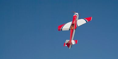 Red and white model airplane flying upwards.