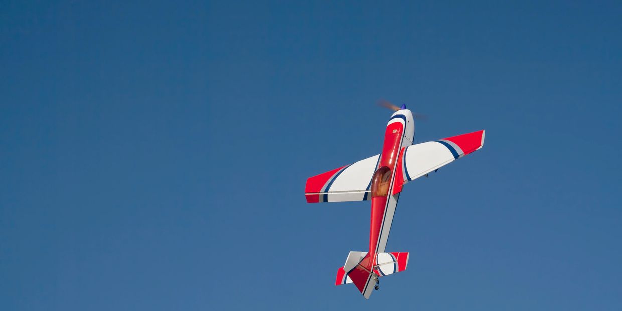 A red and white stunt plane flying vertically against a clear blue sky.
