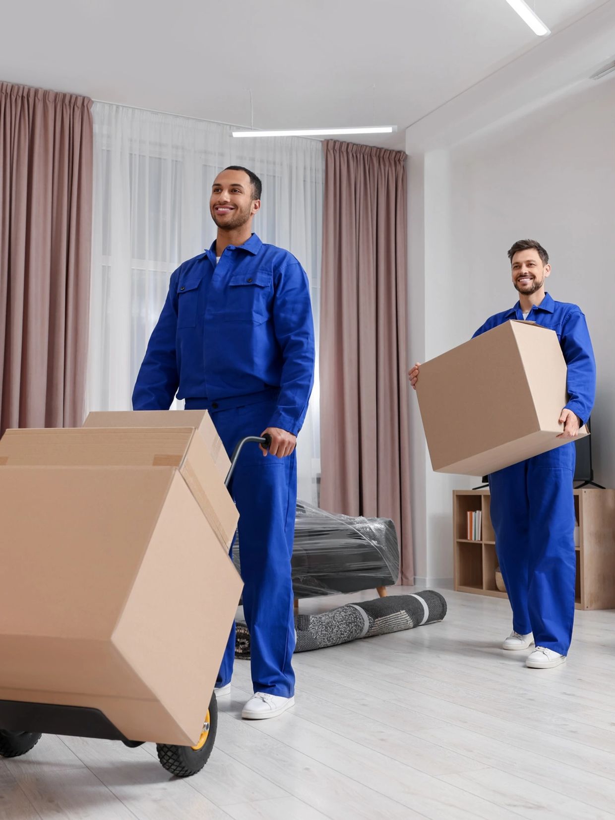 Two movers in blue uniforms carrying cardboard boxes indoors.