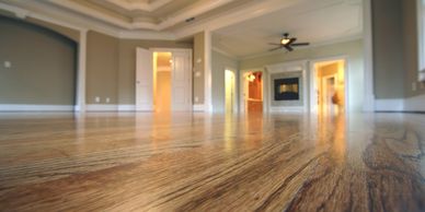 Polished wooden floor in a spacious, empty living room with ceiling fan and fireplace.