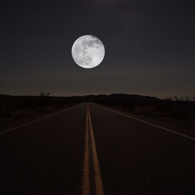 Dark desert highway below a full moon.