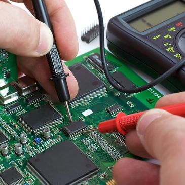 Hands testing a circuit board with a multimeter.