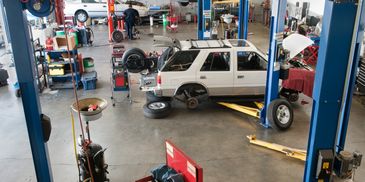 Mechanic in blue uniform inspecting and noting details on a clipboard near a car tire.