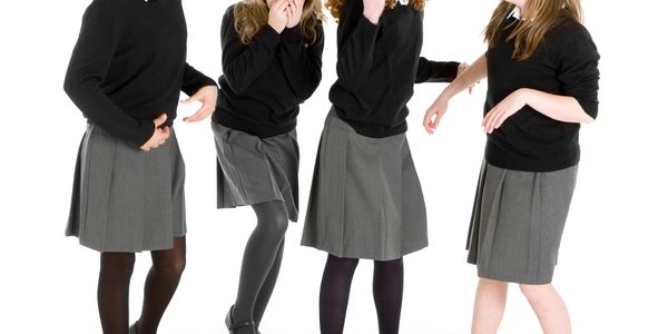 Four girls in school uniforms laughing and reacting to something funny.