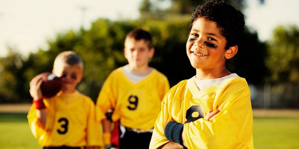 Young boys in yellow football jerseys smiling on a sunny field.