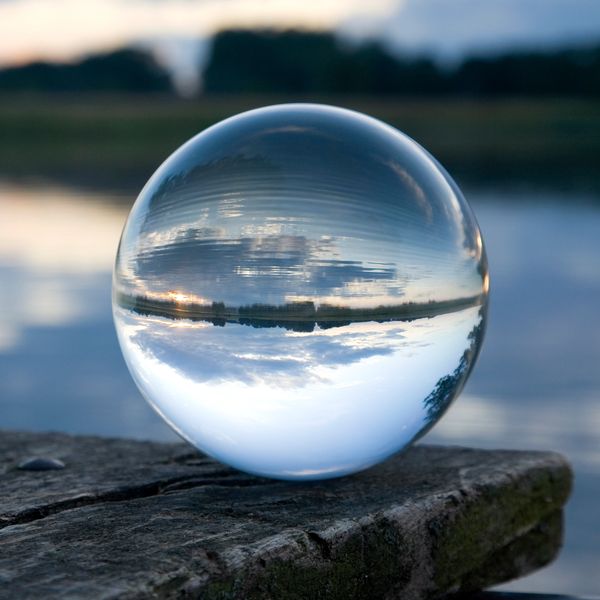 A glass sphere on wood reflecting an inverted lakeside sunset scene.
