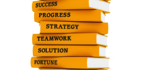 Stack of orange books with motivational business terms on their spines.