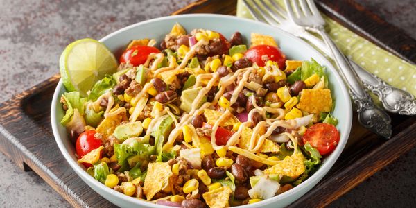 A colorful taco salad with beans, corn, tomatoes, lettuce, and a lime wedge.