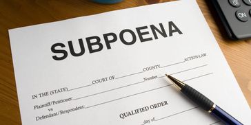 A blank subpoena form with a pen and calculator on a wooden table.