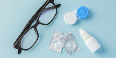 Eyeglasses, contact lenses, case, and eye drops on a blue surface.