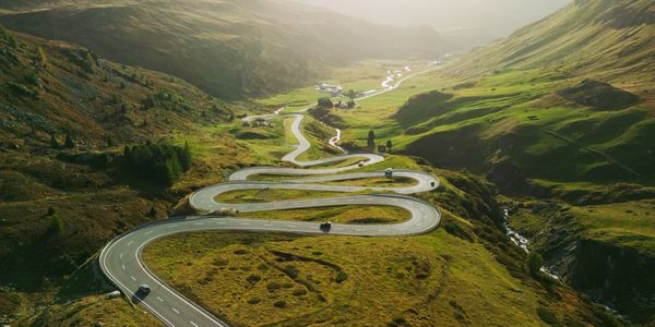 A winding mountain road cutting through lush green hills on a sunny day.