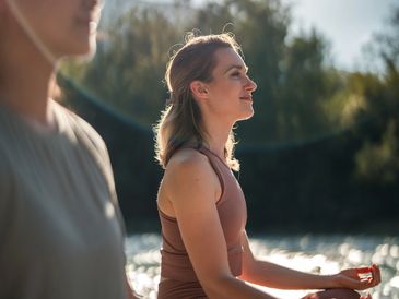 Two women meditating outdoors near water.