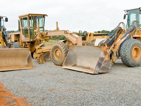 Three large construction loaders parked on gravel.