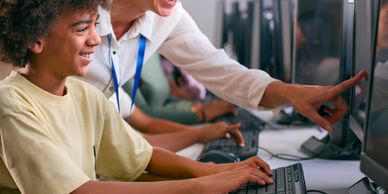 Teacher helping student on computer in classroom.
