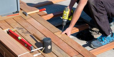 Person installing wooden decking with drill.