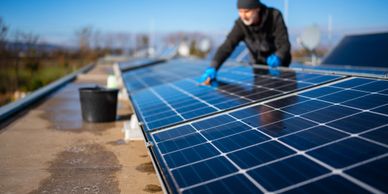 Worker in safety gear cleaning debris from a roof gutter outdoors.