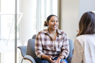 Young woman in plaid shirt smiling during a conversation indoors.