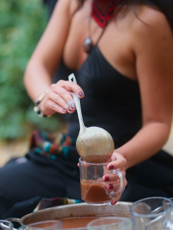 A person pouring hot chocolate into a glass using a ladle.