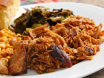 Plate of pulled pork with sides of greens, corn, and bread.
