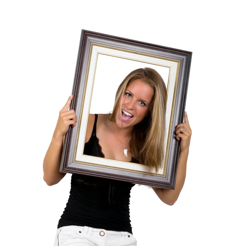 Portrait of beautiful young girl smiling and holding picture frame on white background