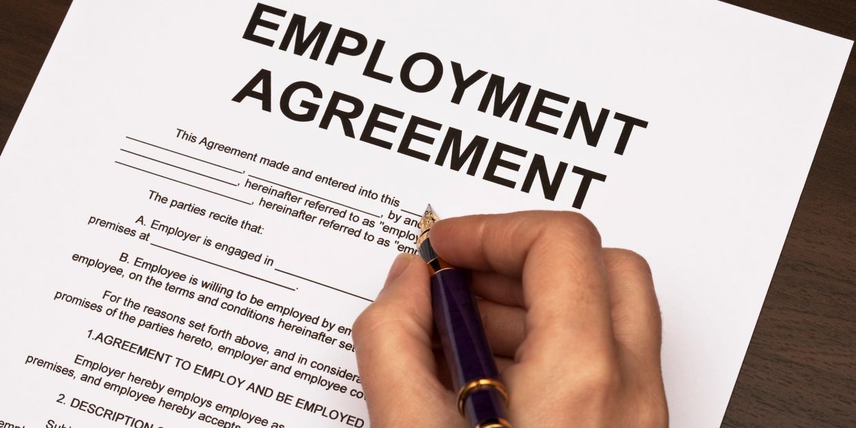 Person signing an employment agreement with a pen.