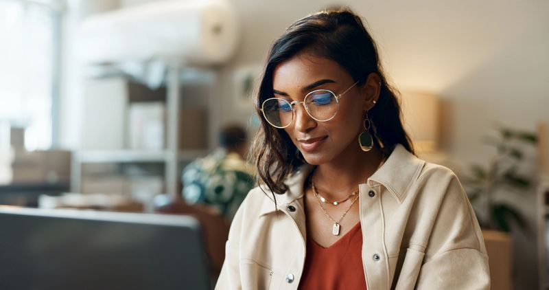 Ecommerce, woman and typing on laptop at work for research, feedback and supply chain for business. Indian, person and planning on pc for logistics, stock administration or package distribution data