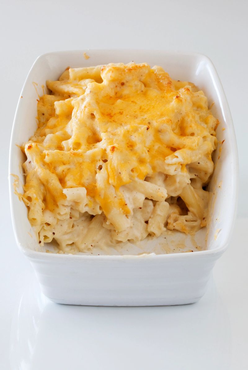 "Baked and grilled Macaroni and cheese in a white oven dish, with a missing portion."