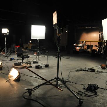A dimly lit film or photography studio with lighting equipment and cables scattered.