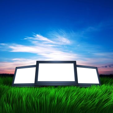 Three blank digital screens on lush green grass under a vibrant blue sky.