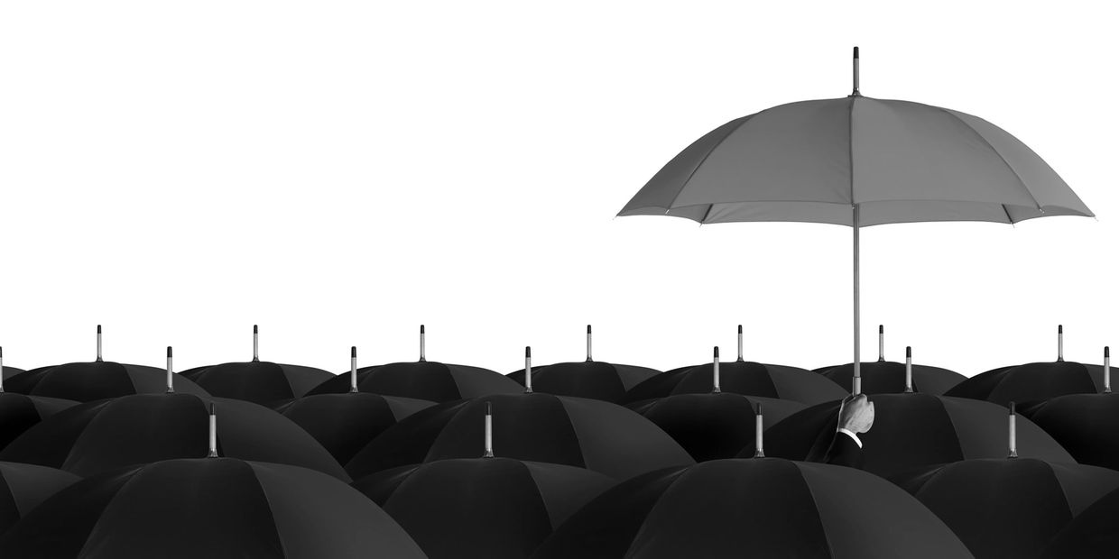 A single red umbrella stands out among many black umbrellas.