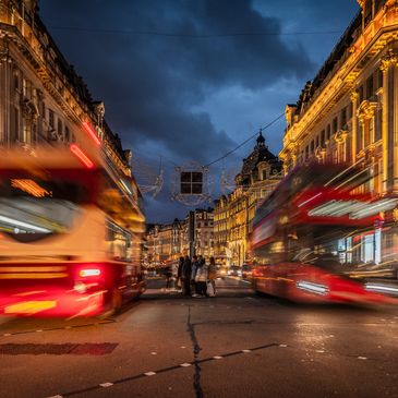 Blurred red double-decker buses in a bustling city street at dusk.