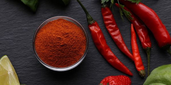 Bowl of chili powder with red chili peppers and lemon on a dark surface.