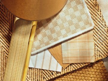 Swatches of beige and brown fabrics and woven materials arranged with a wooden paddle.