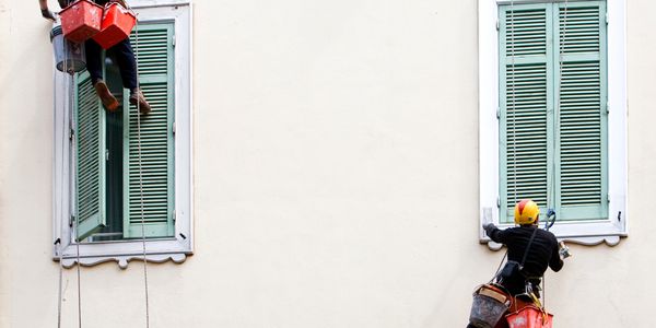 Two workers suspended by ropes cleaning or painting windows on a building.