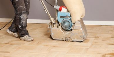 Worker using a floor sanding machine on wooden parquet flooring.