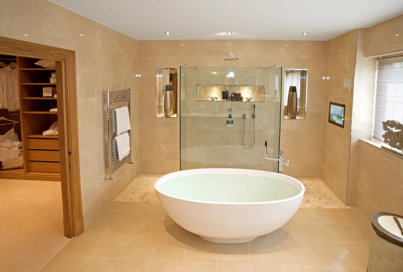 an elegant master bathroom in an expensive new luxury home. An unusual oval bath full with hot water sits in the middle of the room.  The decor has been tastefully prepared by a leading Interior Designer.