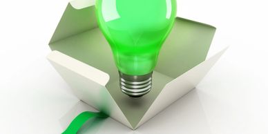 A green light bulb emerging from an open box with green ribbon.