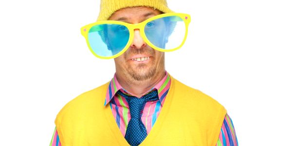 Man wearing oversized yellow sunglasses and colorful clothes with a yellow hat.