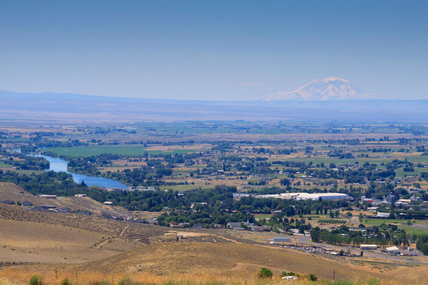 A town with a river and a snow-capped mountain in the background.