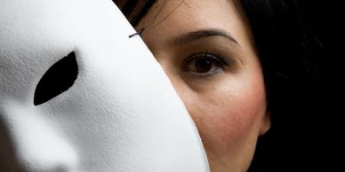 Femme tenant un masque blanc à moitié sur son visage.