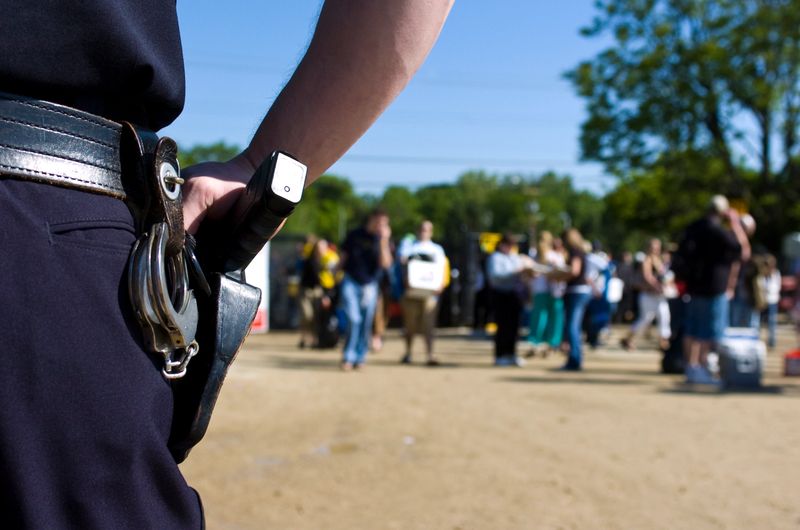 A police officer watches as spectators enter the a large public event, focus on handgun.