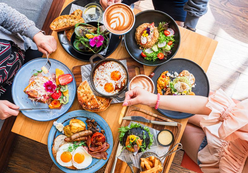 Table top view of breakfast food displayed on table, people eating food.