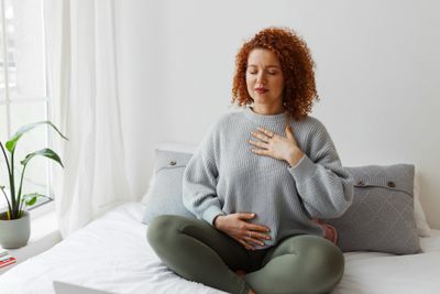 Woman practicing mindful breathing while sitting cross-legged on bed.
