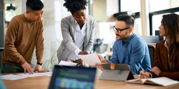 A diverse group discussing documents around a table in an office.