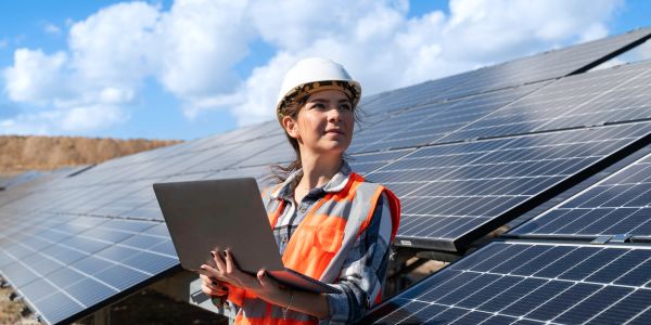 Woman engineer with laptop near solar panels.