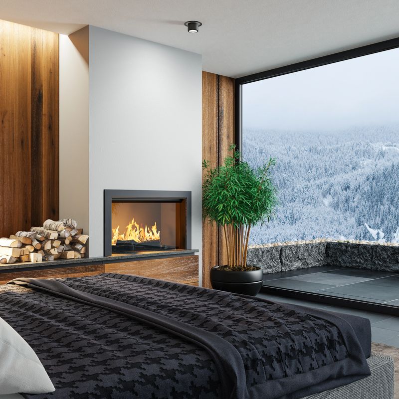 Luxurious bedroom with natural stone, king size bed and and fireplaceBlack and white fireplace on a natural stone wall. Stylish and comfortable bedroom area with a modern bed. Dark gray accent slate stone walls with natural dark wood panels.Natural stone black floor. Ceiling with strip cove lighting and spotlights.