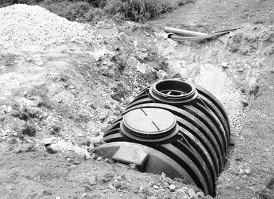 Excavator digging a large hole with a septic tank installation in progress.