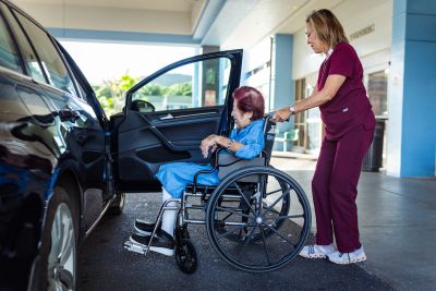 Caregiver helping a woman in a wheelchair to get into a car.
