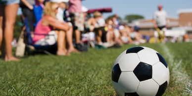 A soccer ball sits on grass with spectators blurred in the background.